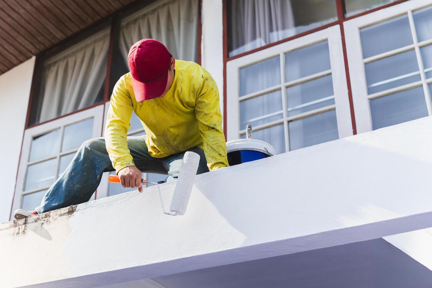 worker painting an exterior wall with a roller during house maintenance free photo
